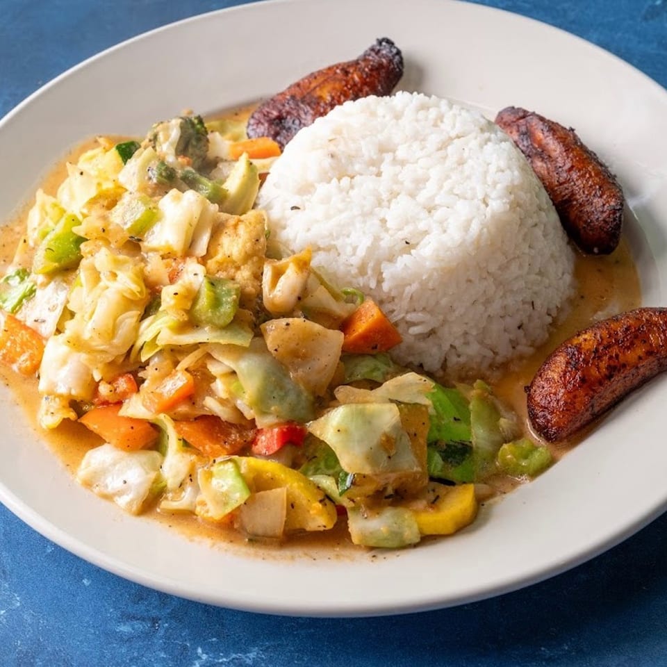 Plate of white rice, creamy mixed vegetables, and fried plantains on a blue tabletop.