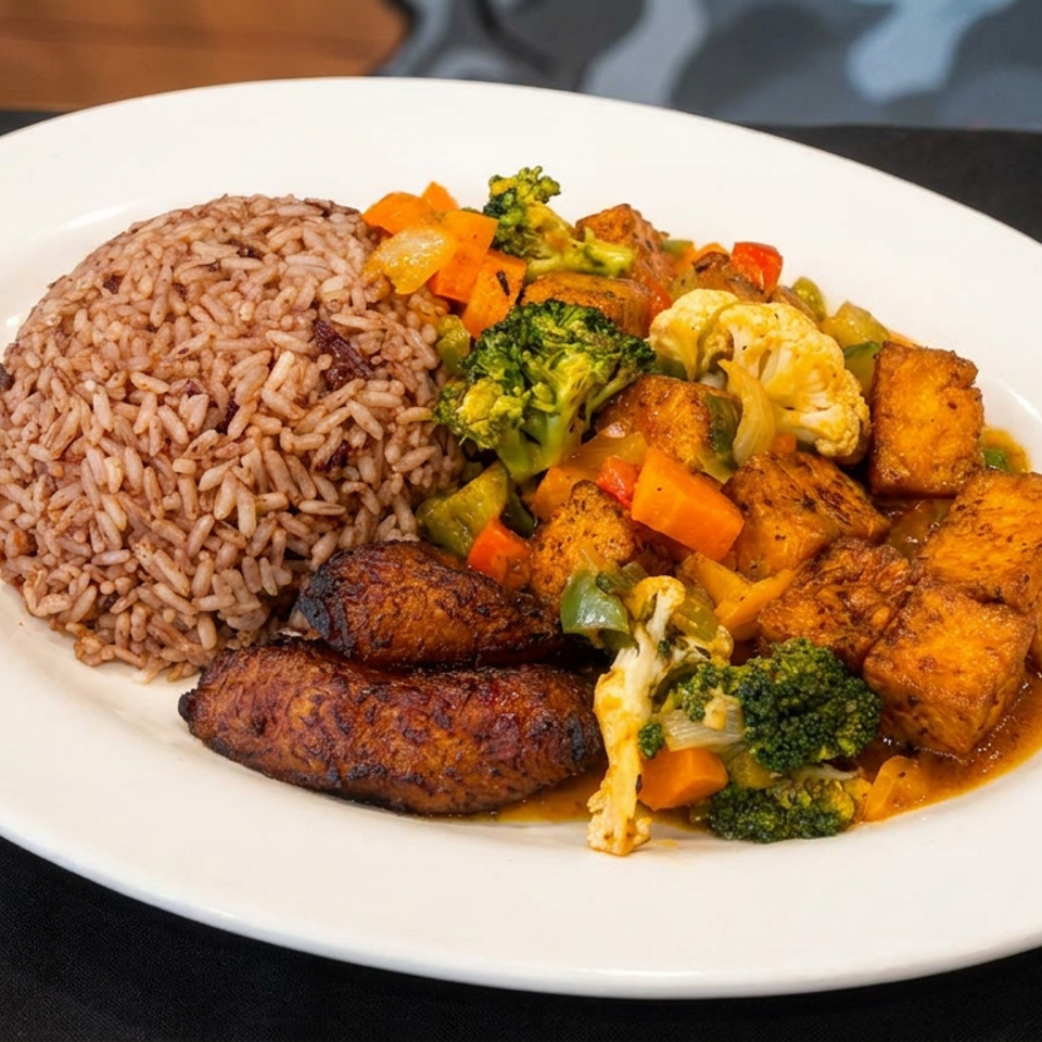White plate featuring seasoned rice, grilled plantains, roasted vegetables, and golden tofu in savory sauce.