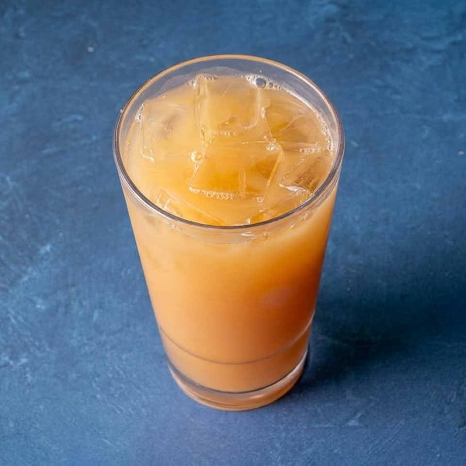 Glass of orange-colored iced beverage on a textured blue surface.
